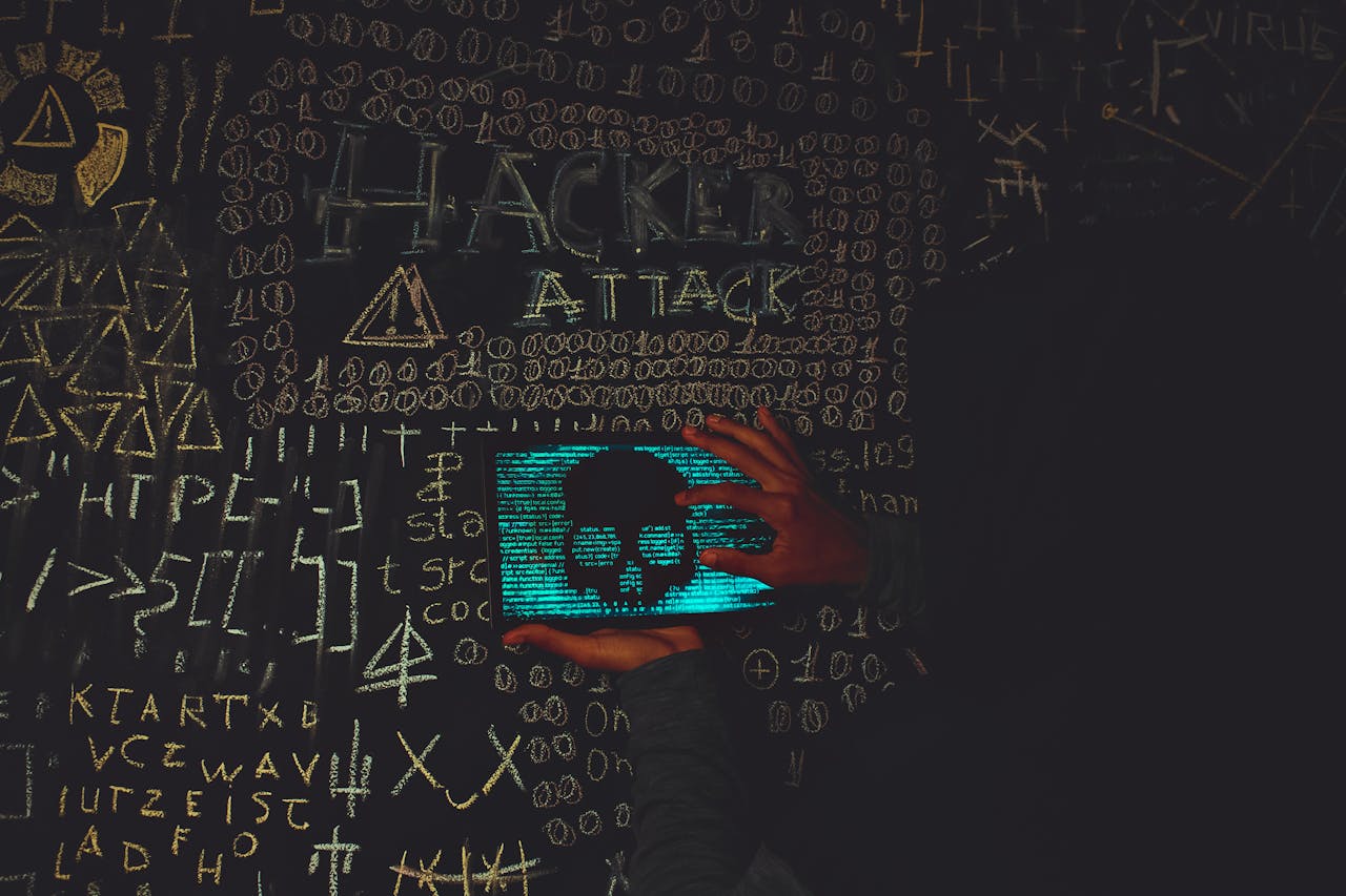 A hacker in a black hoodie using a tablet displaying a skull, surrounded by chalk symbols and 'Hacker Attack' text.